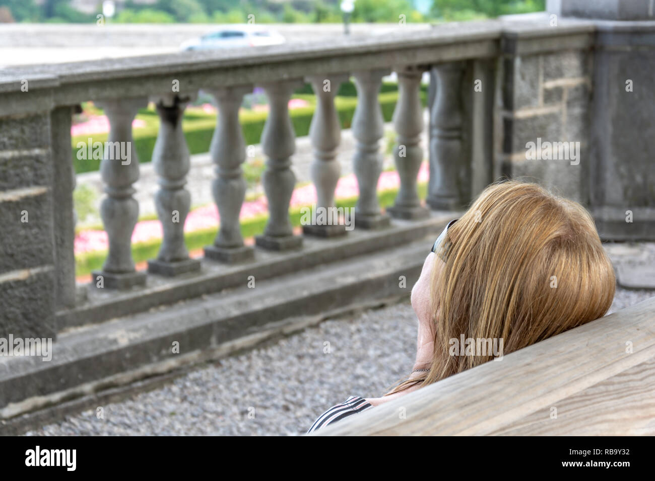 A vision of a blond woman's head with sun glasses in front of a concrete decorative low wall Stock Photo