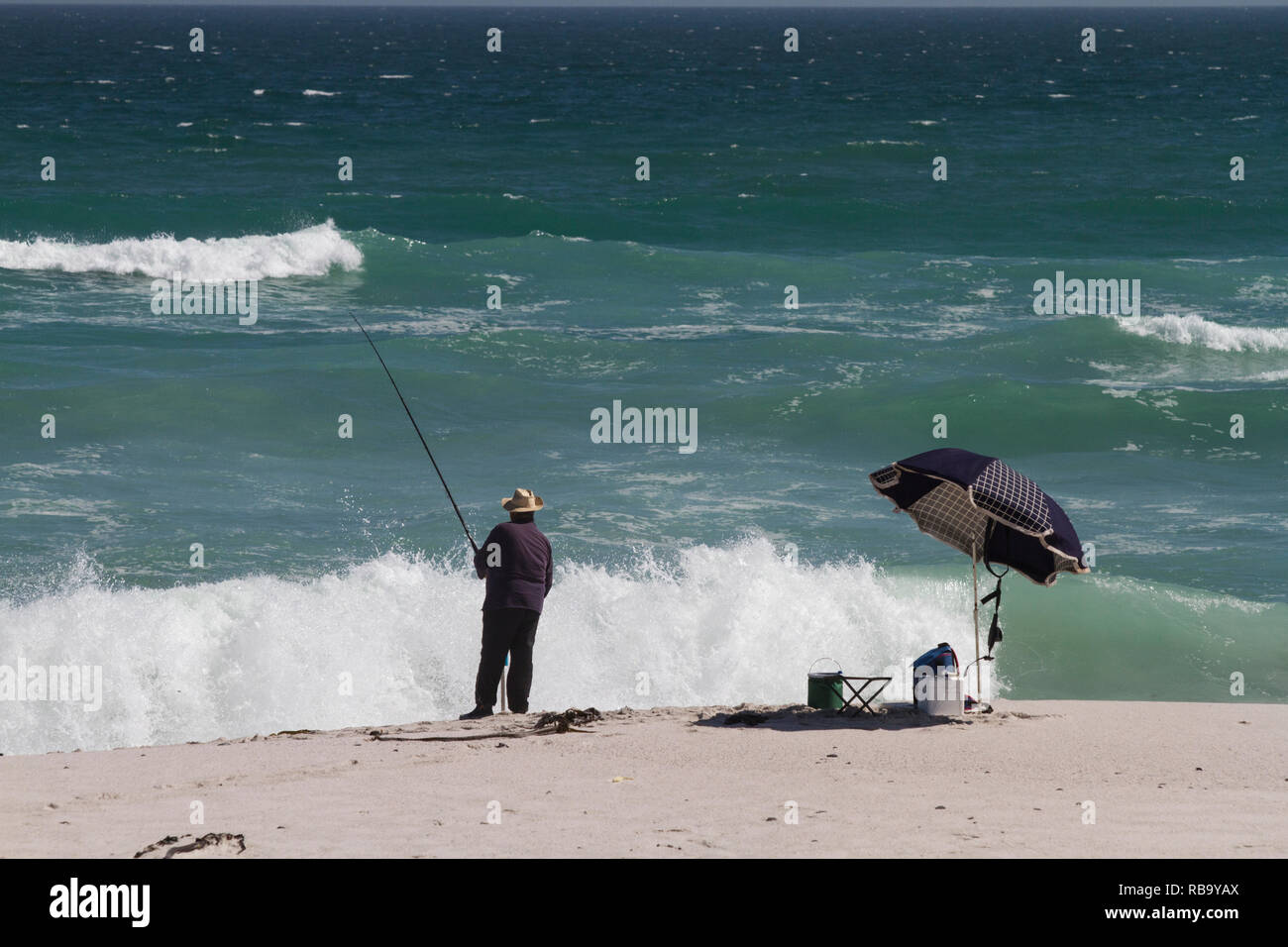 Fisherman on the beach, next to umbrella Stock Photo