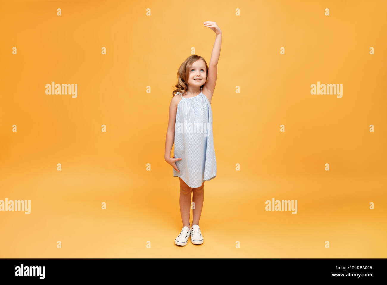 A little child measures her height on a yellow background. Concept of development, goal, success Stock Photo