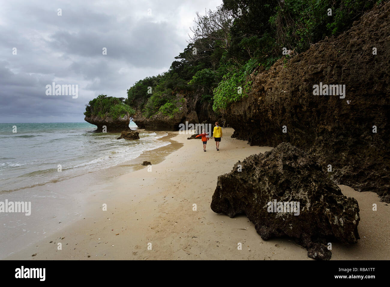 Mother and son walking on dramatic sandy beach with limestone scultures at Ibaruma Sabichi Cave, Ishigaki, Japan Stock Photo