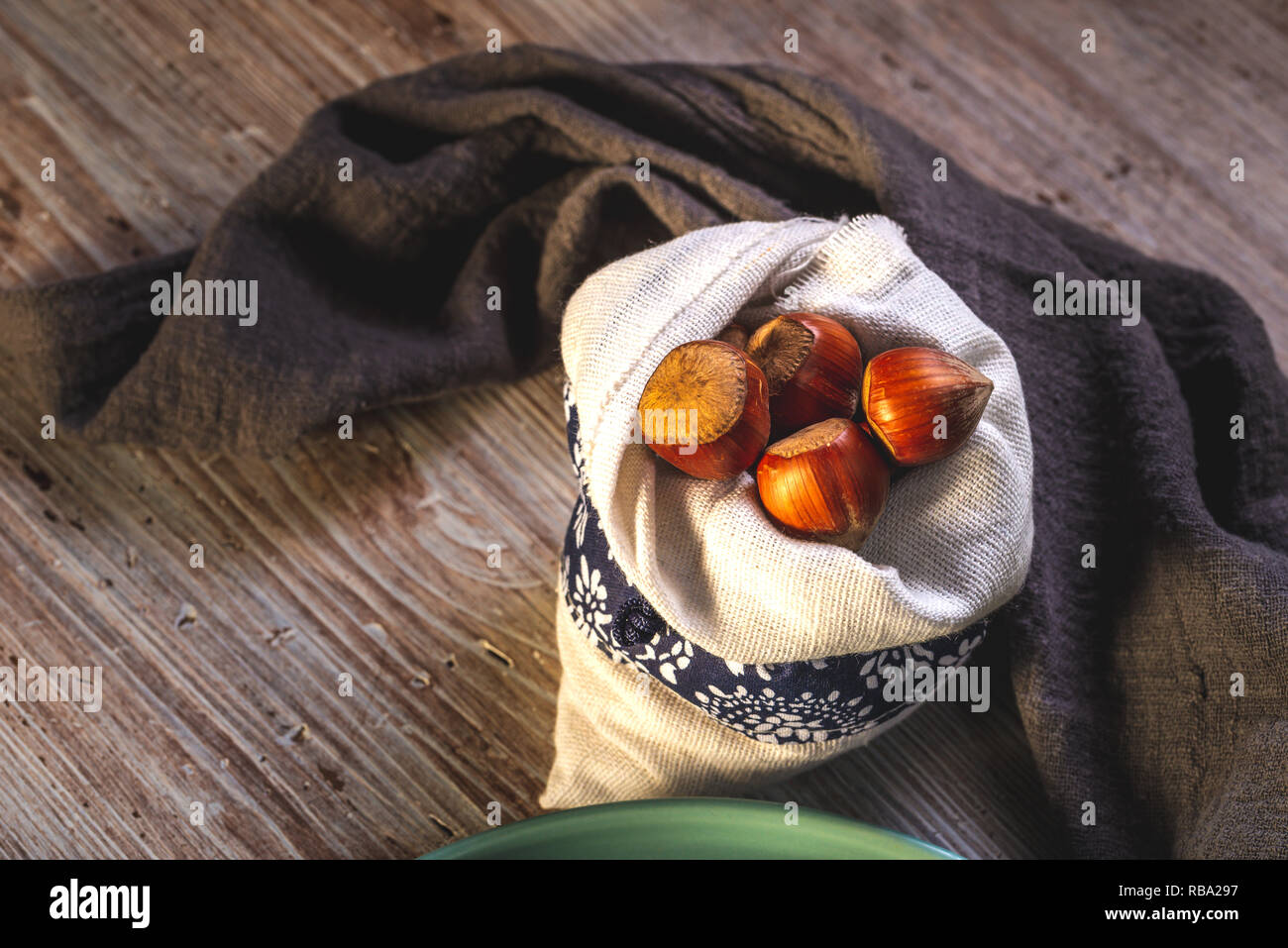 Horizontal photo with several nuts. Hazelnuts are placed in white linen bag with blue ornament. Bag is placed on wooden board with white and brown vin Stock Photo