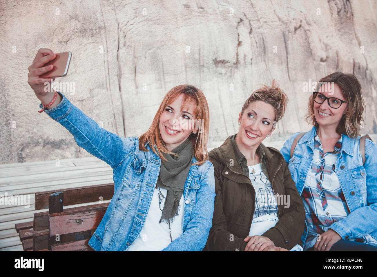 Three Happy Young Women With Winter Clothing Sitting On A Wooden