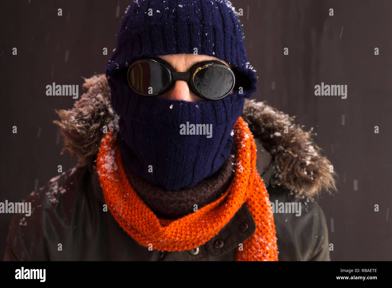 Portrait of a single male winter adventurer wearing a warm green coat with fur hood, a blue ski cap, an orange scarf and black retro style goggles Stock Photo