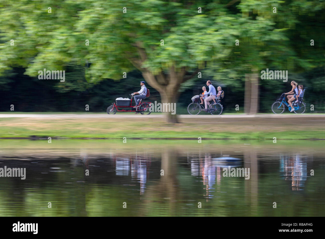 The Netherlands, Amsterdam. Vondelpark. Parents bring their children to school by bicycle, others go to work. Blurred motion. Stock Photo