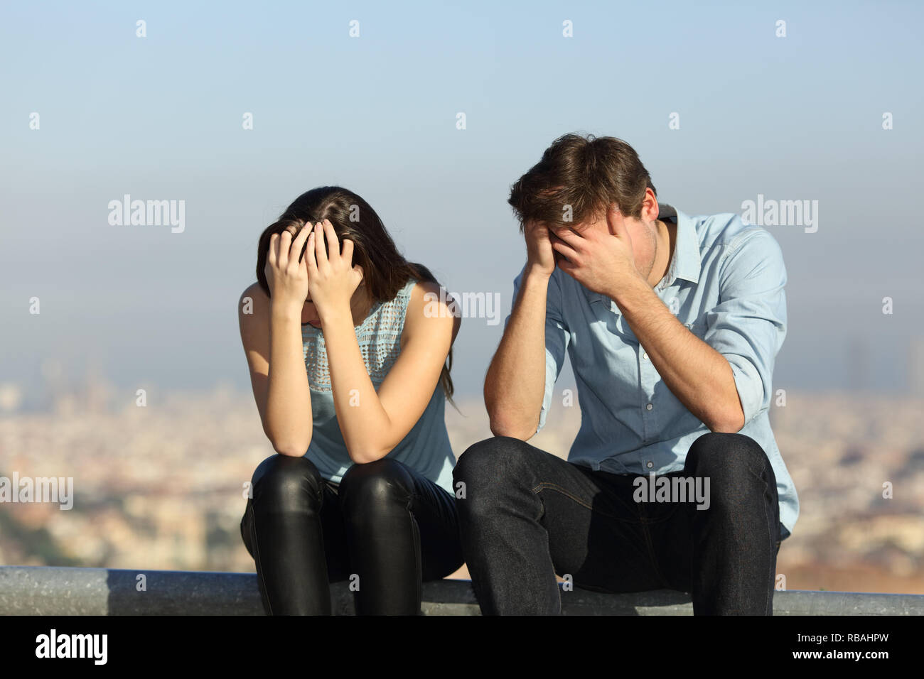 Sad couple complaining after argument sitting outdoors in a city ourskirts Stock Photo