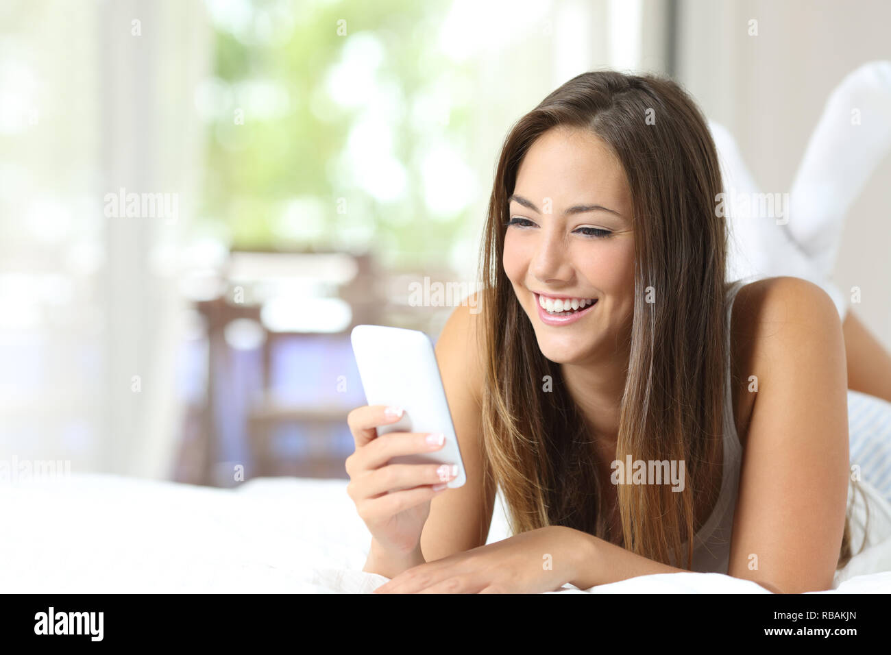 Happy girl lying on the bed using a smart phone at home Stock Photo - Alamy