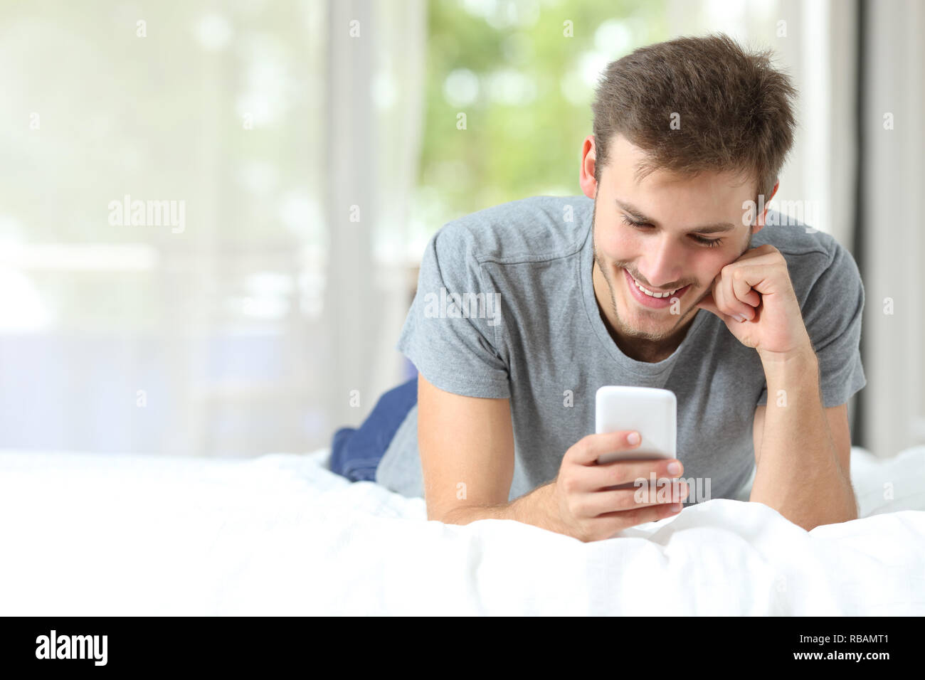 Front view portrait of a single man checking smart phone on a bed at hotel room Stock Photo