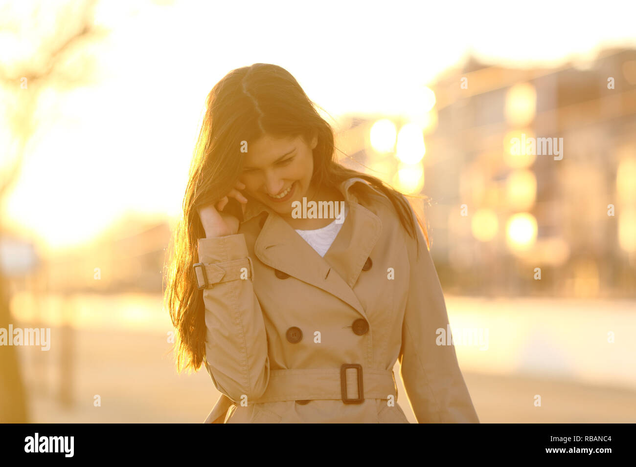 Front view portrait of a candid woman talking on phone at sunset in the street Stock Photo