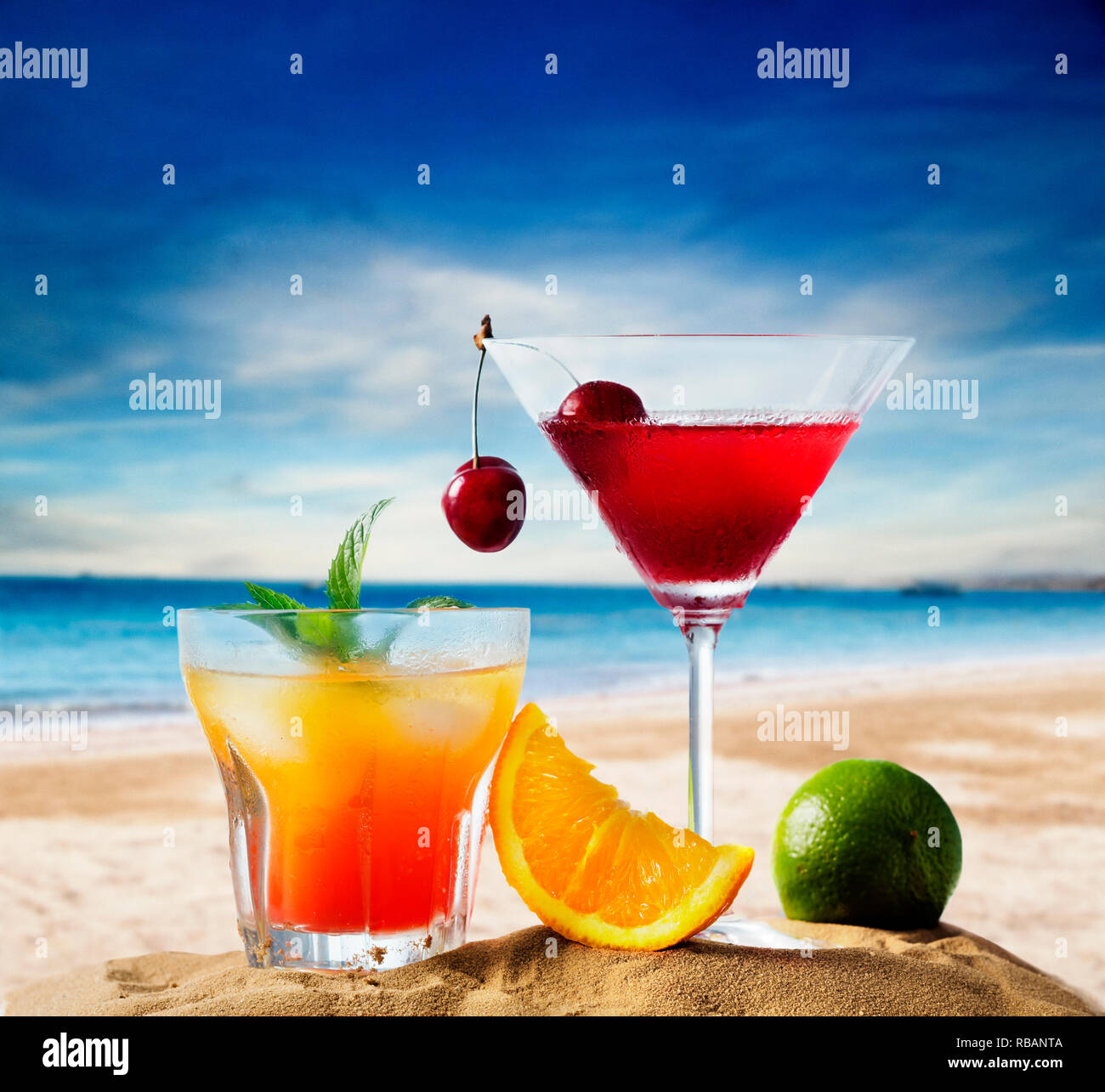 Cherry cocktail in martini glass and orange juice vodka on tropical sandy beach. Summer holiday and beach party design. Stock Photo