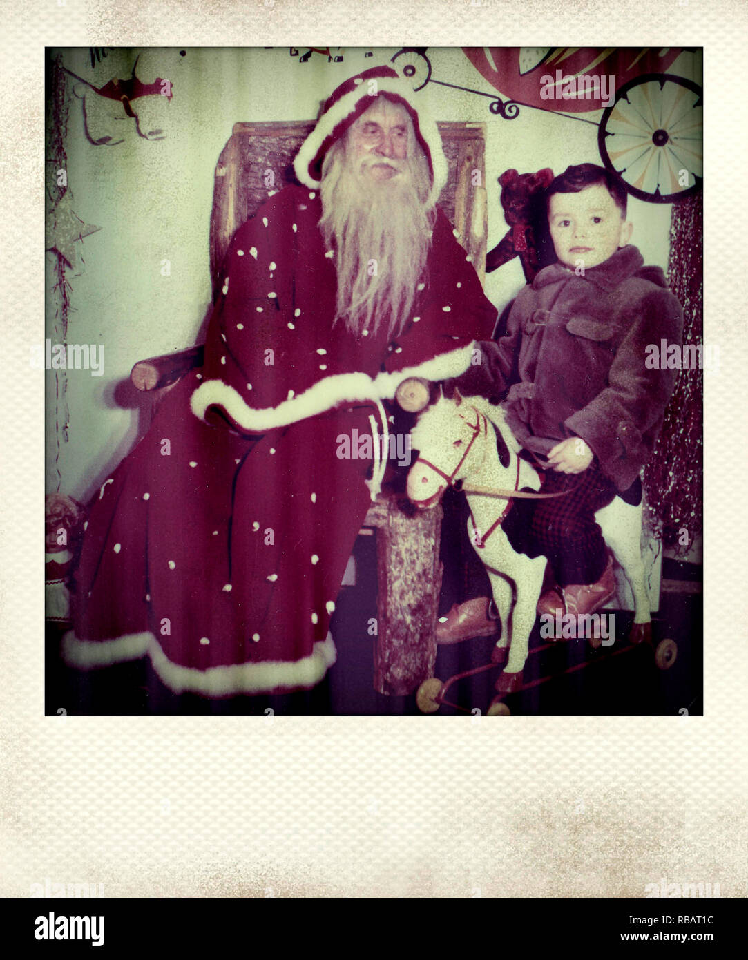 Photograph of a small boy riding a rocking horse next to Santa Claus Stock Photo