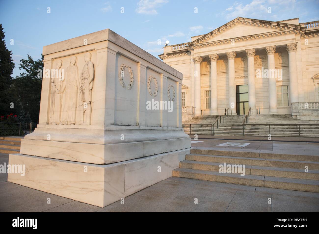 Color photograph of the East and North facing panels of the Tomb of the Unknown Soldier, shot from a low angle, with a bas-relief carving depicting the Classical allegorical figures Peace, Victory, and Valor visible on the East side, wreaths visible on the North side, and with the eastern entrance to the the Arlington Memorial Amphitheater in the background, located at Arlington National Cemetery, in Arlington, Virginia, USA, image courtesy Elizabeth Fraser and the Arlington National Cemetery, August 7, 2018. () Stock Photo