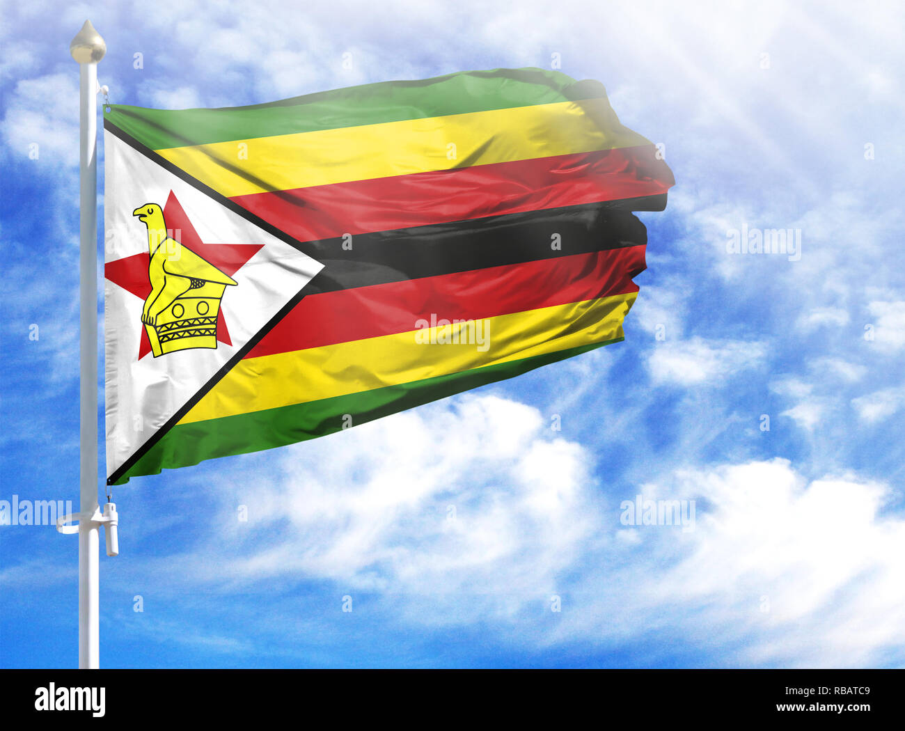 National flag of Zimbabwe on a flagpole in front of blue sky. Stock Photo