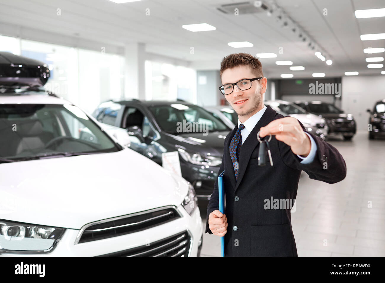 The seller of cars with the keys in hand in the auto showroom. Stock Photo