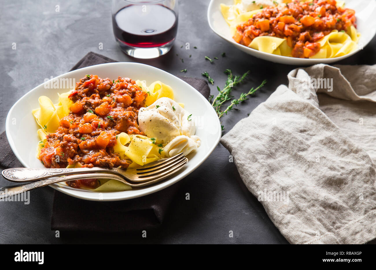 Pappardelle pasta with meat ragout with pumpkin and burrata cheese on gray concrete background. Italian cuisine. Stock Photo