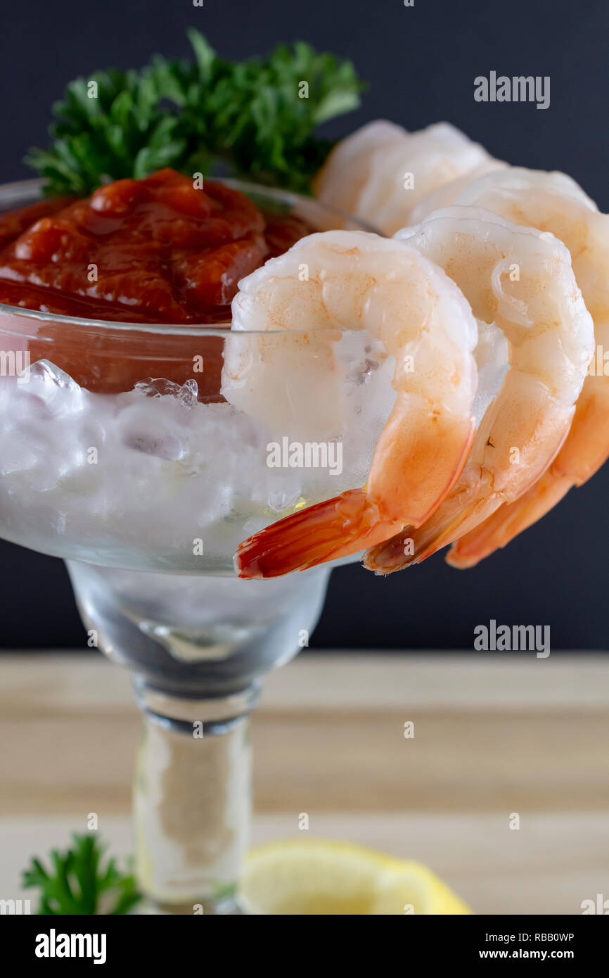 Shrimp cocktail in margarita glass.  Selective focus on shrimp hung on side.  Parsley and cocktail sauce in cup with ice.  Lemon and parsley at base o Stock Photo