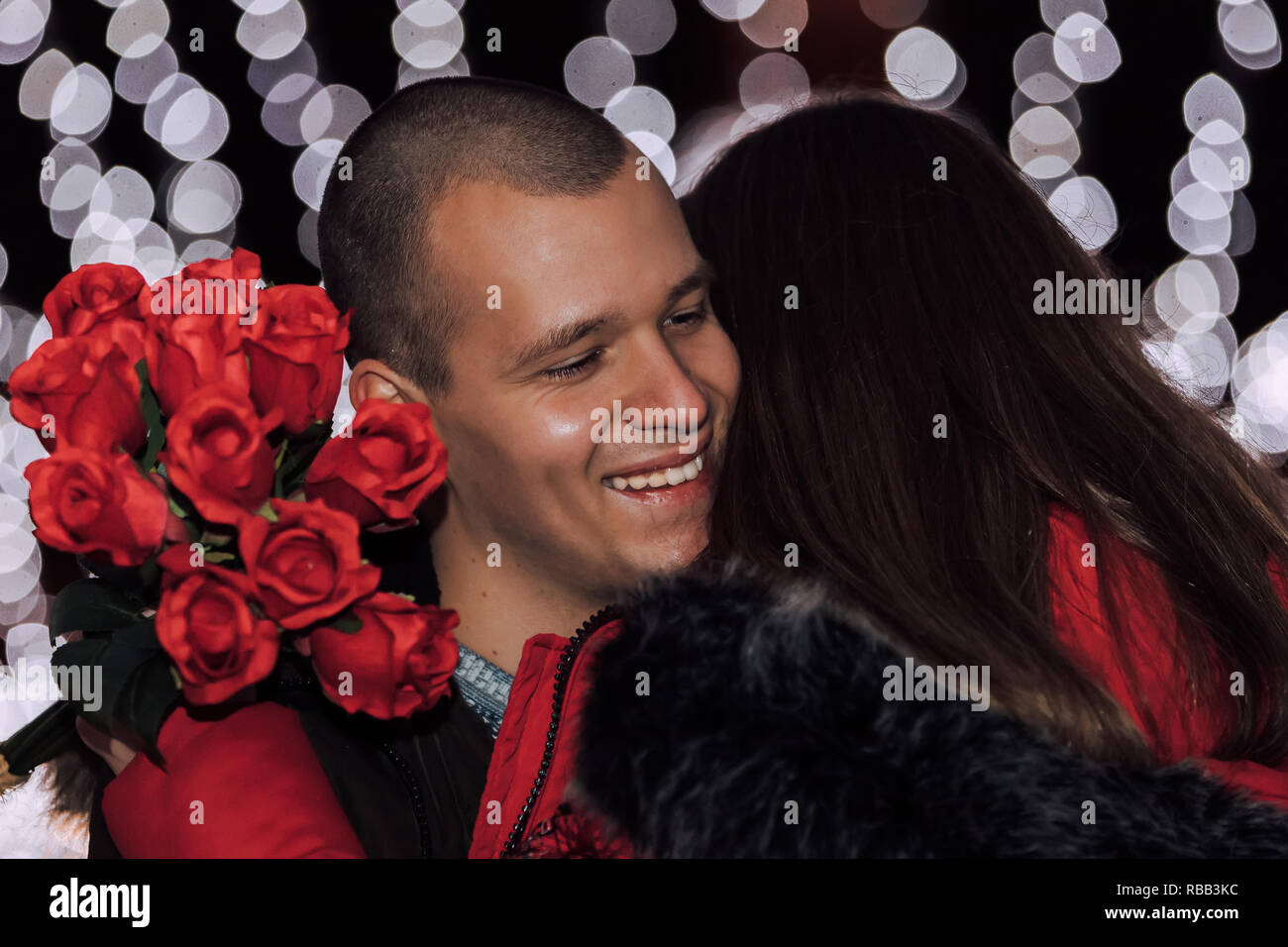 Valentine's day or anniversary concept - man giving a bouquet of roses from his surprised girlfriend at winter night in the city street. Close up Stock Photo