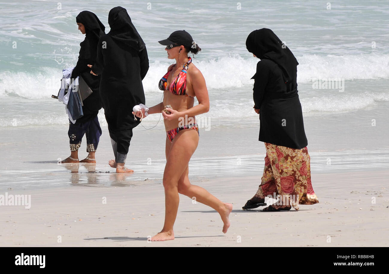 Licensed to Andrew Parsons / Parsons Media. 14/05/2009. Dubai, UAE. A woman  in a bikini walks past a ladies in an Abaya on a beach in Dubai as summer  arrives. Temperatures have