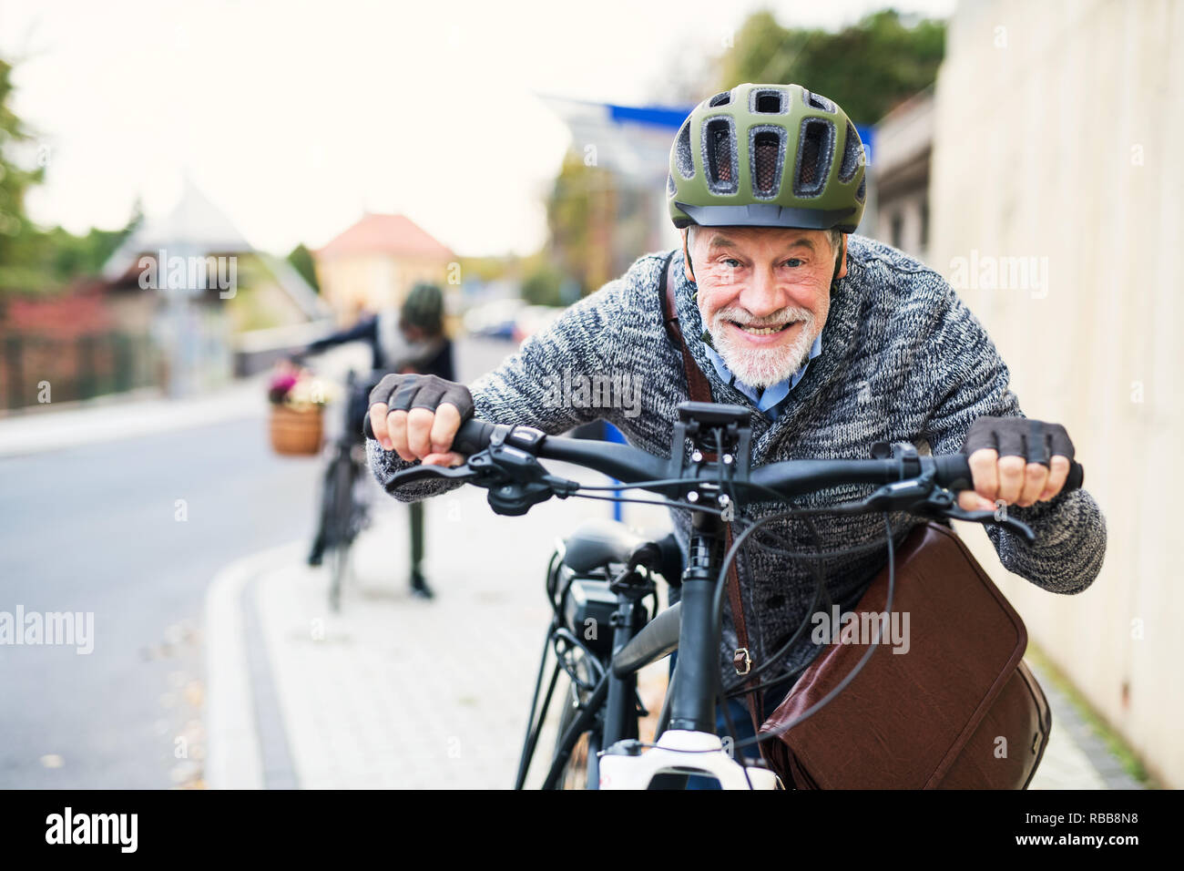 Active senior couple with electrobikes standing outdoors on a road in town. Stock Photo