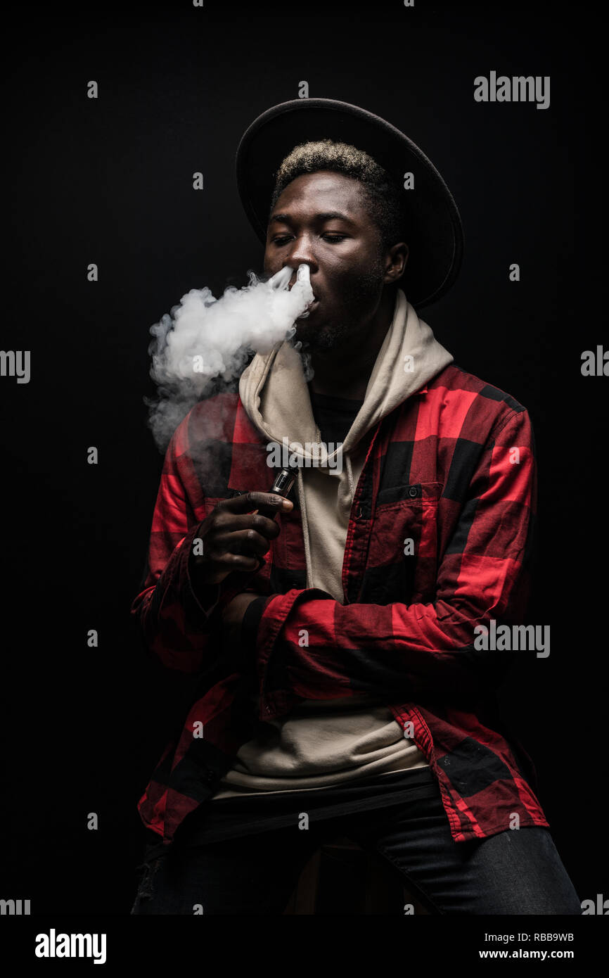 Young thinking serious concentrated african man standing and smoking electronic cigarette isolated on gray background Stock Photo