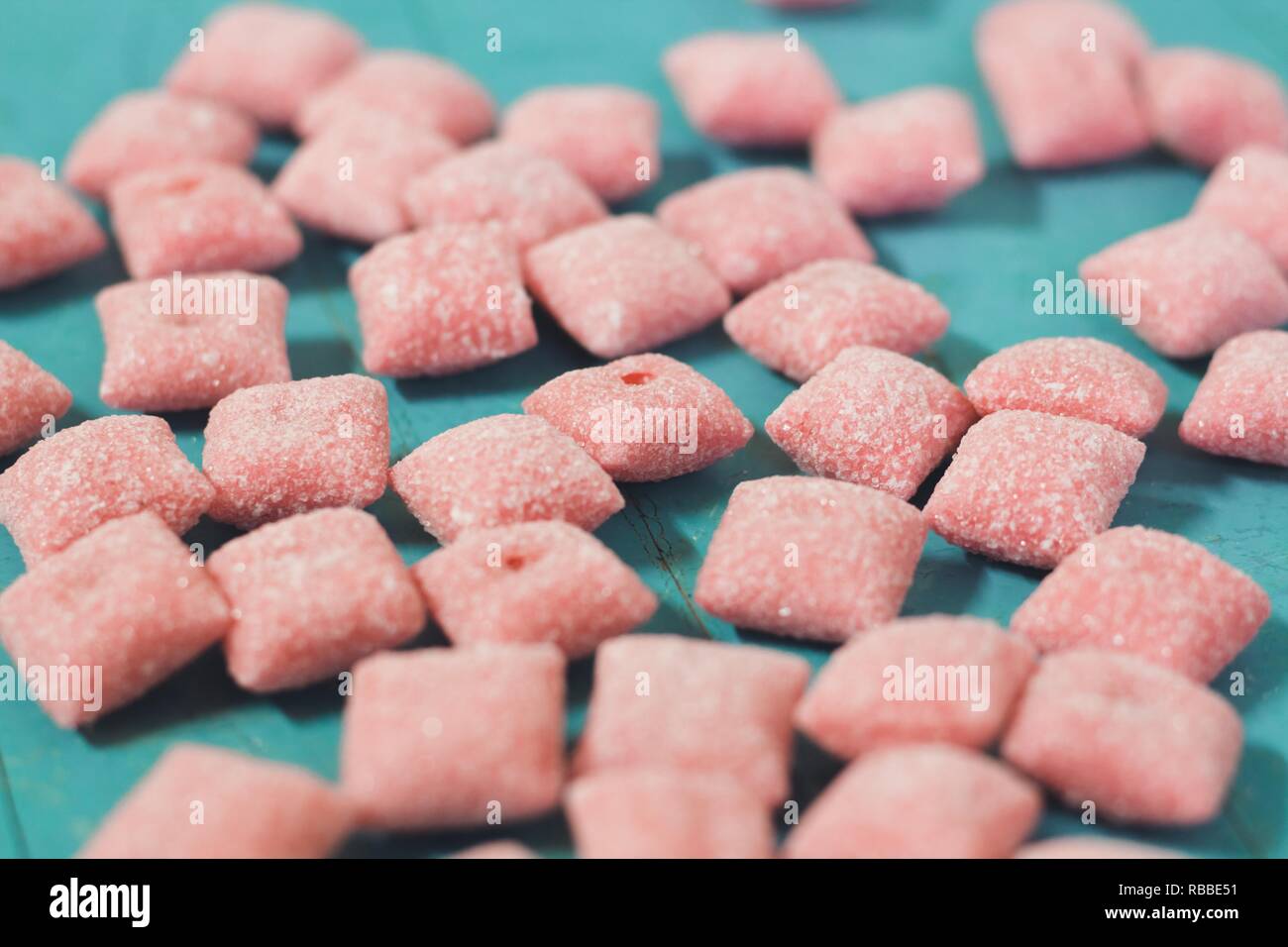 Red hues square sugar candies. Candies lie on the wooden surface of the blue otyaenok. Very tasty and sweet candy. Stock Photo