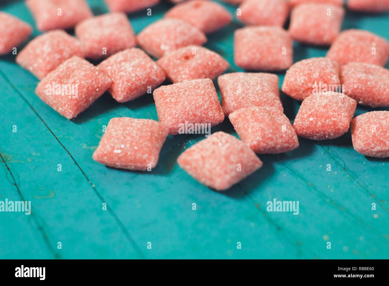 Red hues square sugar candies. Candies lie on the wooden surface of the blue otyaenok. Very tasty and sweet candy. Stock Photo