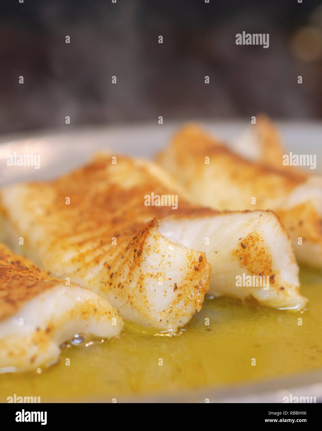 Three  baked grilled fish fillets in butter on plate steaming on restaurant grill.  Macro close up shot. Stock Photo