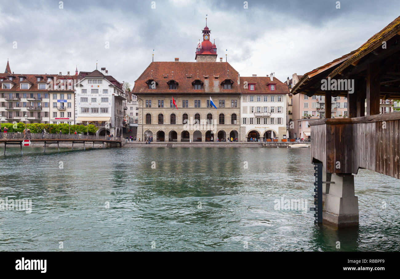 Lucerne, Switzerland - May 7, 2017: Cityscape of Lucerne city with town hall and wooden bridge over Reuss river. Ordinary people walk the embankment Stock Photo
