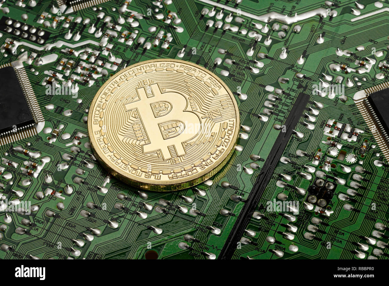 A Bitcoin coin resting on a printed circuit board Stock Photo