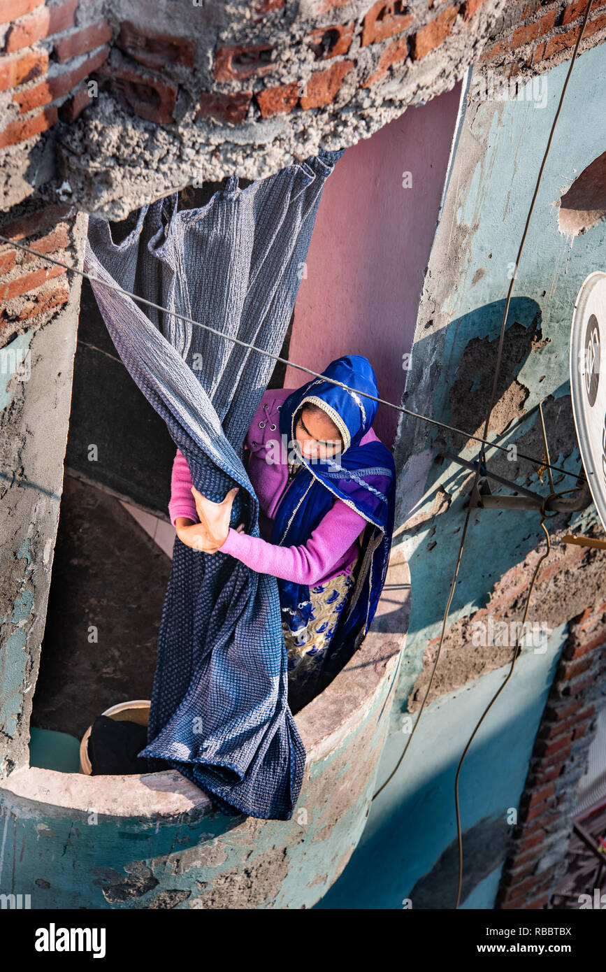 A woman looks down from a balcony clutching at the curtain in JJ Colony Madanpur Khadar, New Delhi Stock Photo