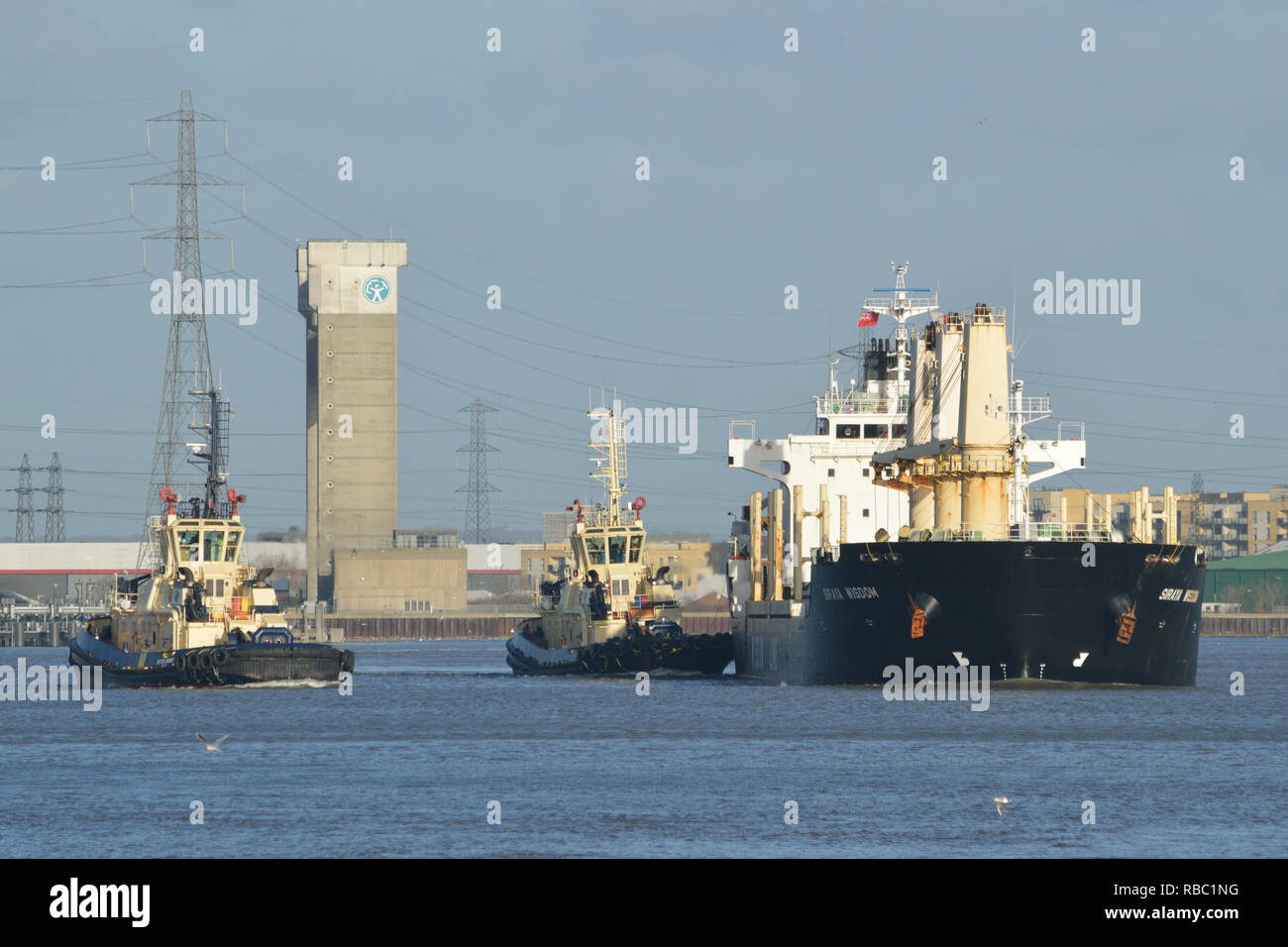 Two Svitzer Global tugs help bulk carrier Siraya Wisdom prepare to moor at a berth on the river Thames in London Stock Photo