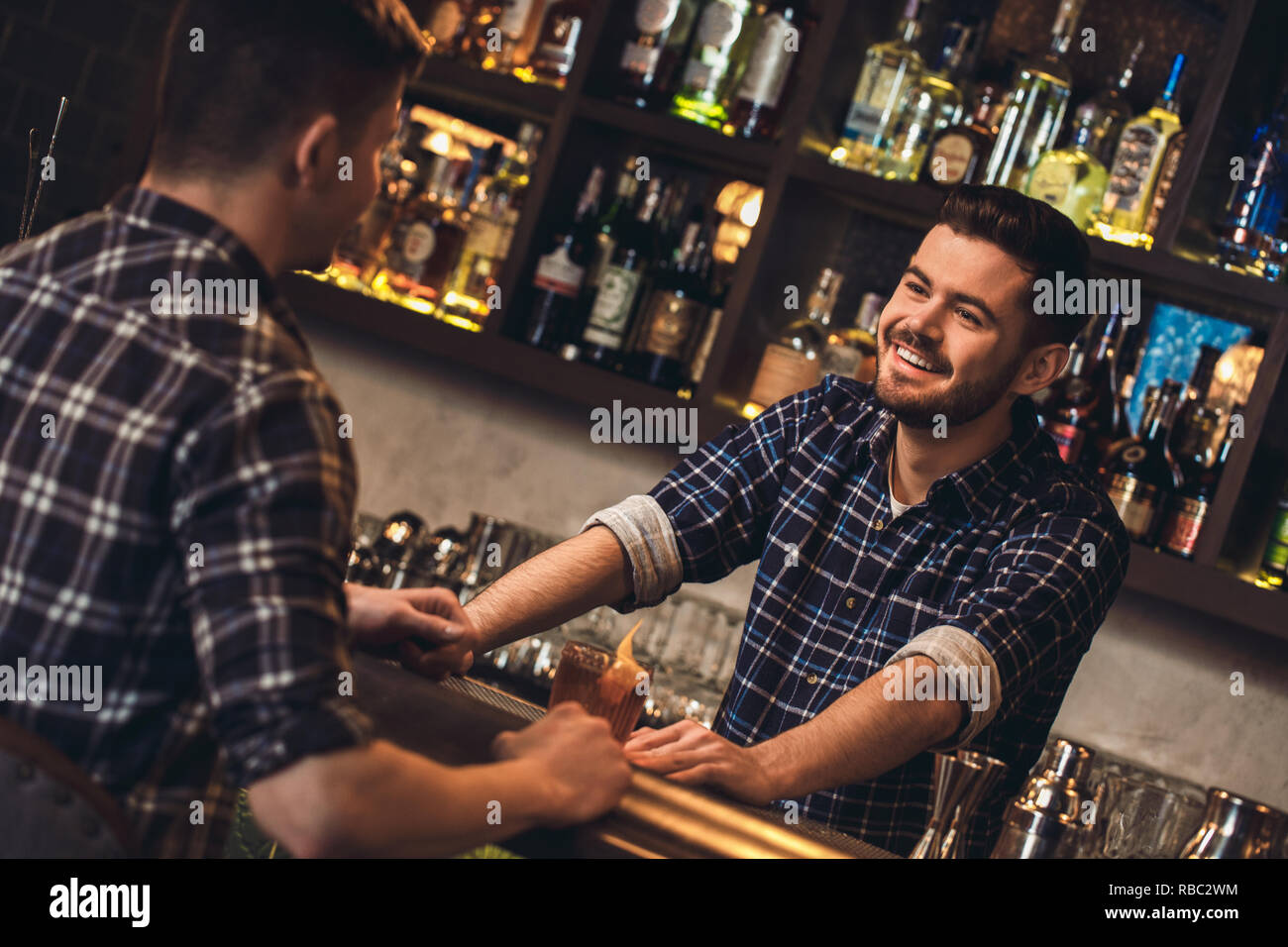 Young barman standing at bar counter with customer drinking cocktail ...