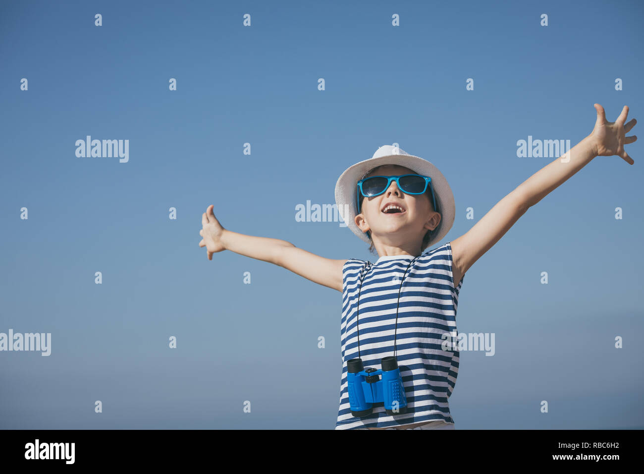 One happy little boy playing on the beach at the day time. He are dressed in sailor's vest. Kid having fun outdoors. Concept of sailor on vacation. Stock Photo