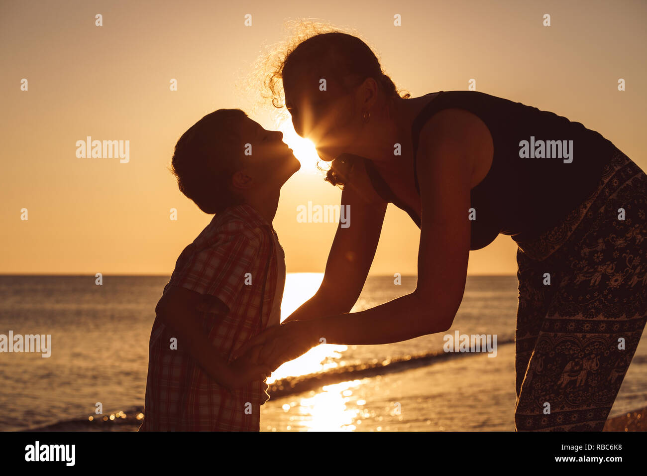 Mother and son playing on the beach at the sunset time. People having fun outdoors.  Concept of happy vacation and friendly family. Stock Photo