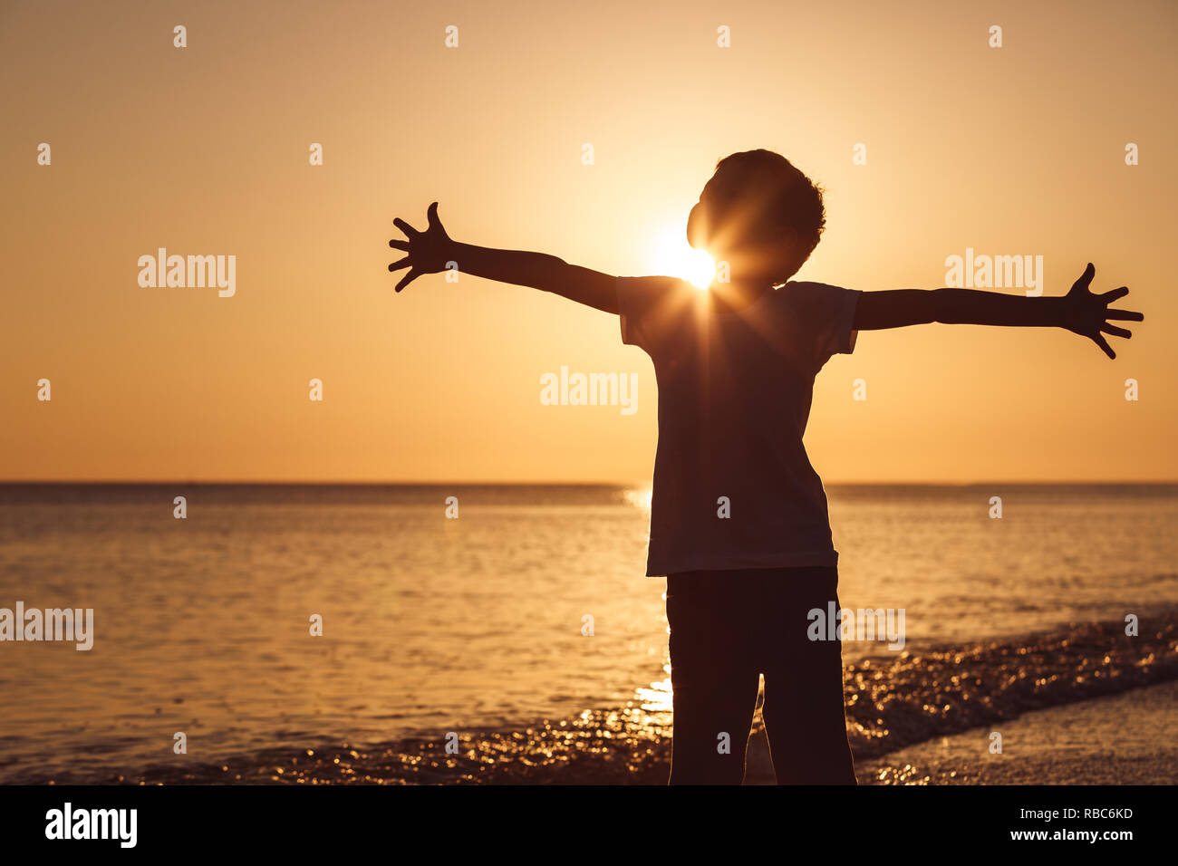 One happy little boy playing on the beach at the sunset time.  Kid having fun outdoors. Concept of summer vacation. Stock Photo