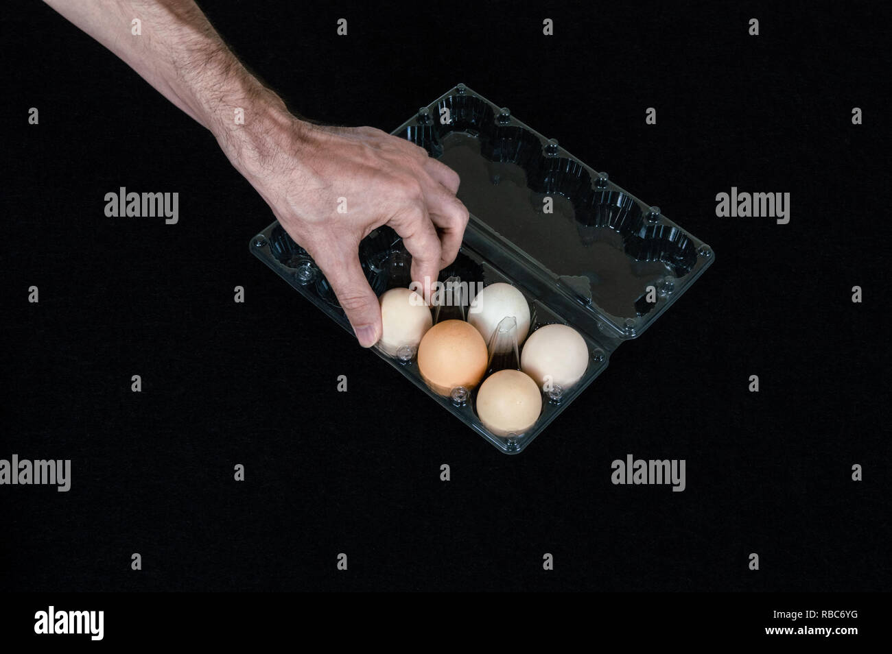 Male hand taking one egg from plastic egg box on black felt background. Stock Photo