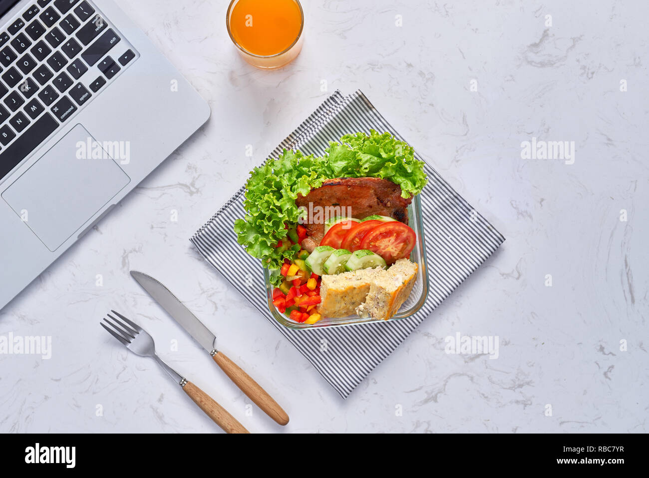 Top view of laptop, orange juice in glass and fresh salad in lunch box