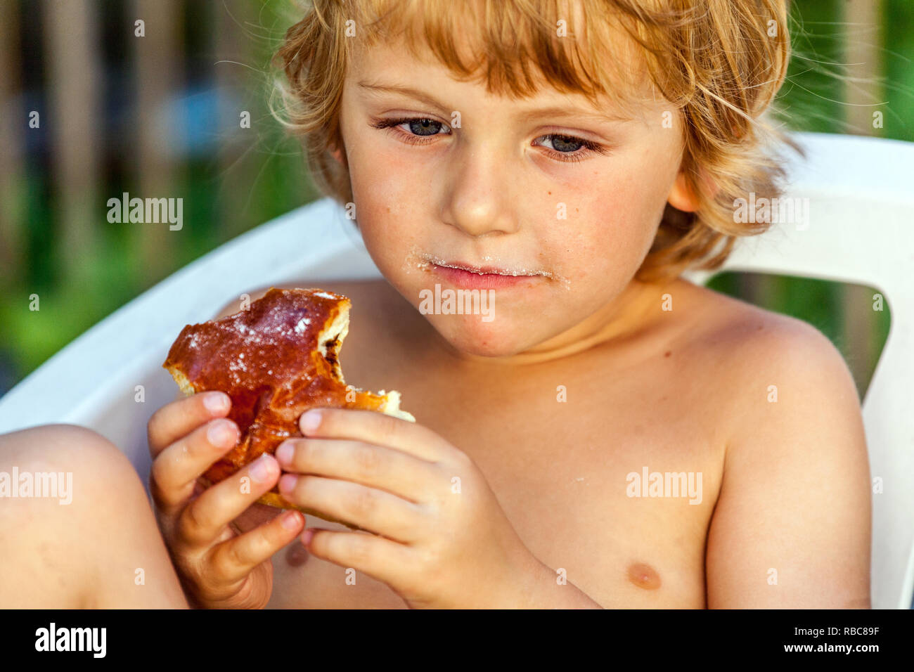 Young blonde boy, toddler eating cake, child eating Stock Photo