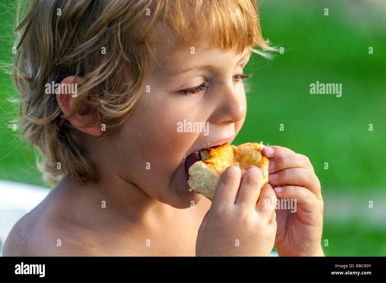Young blonde boy, toddler eating cake, child eating Stock Photo
