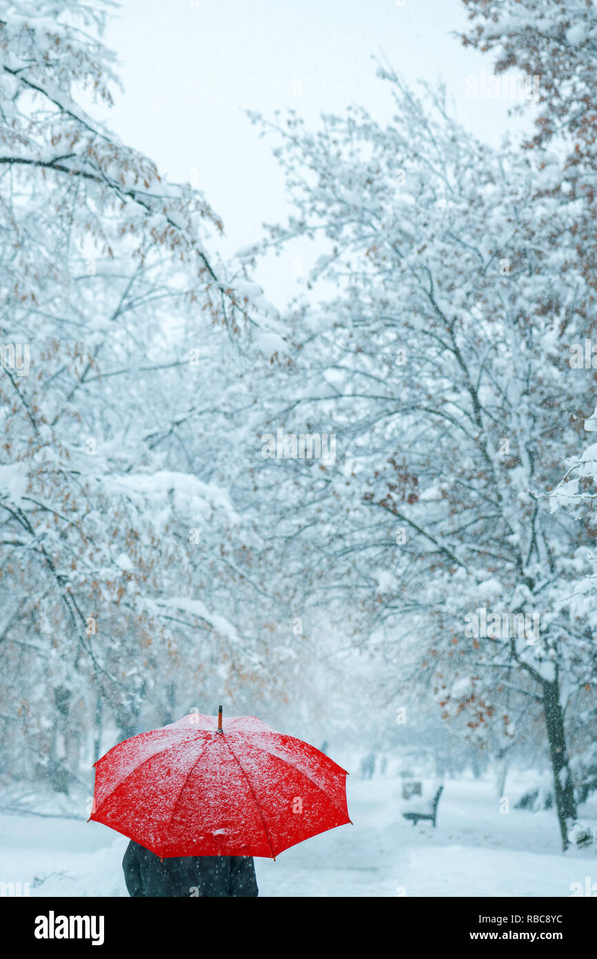Woman under red umbrella in snow enjoying the first snowfall of the