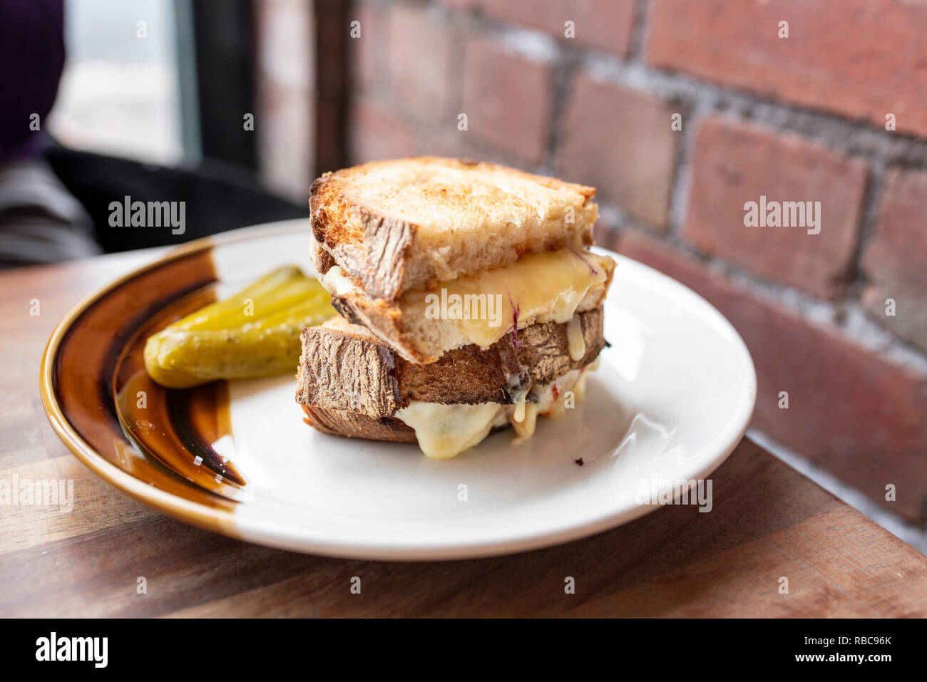 Two melted cheese sandwich halves stacked on top of each other on a white and brown plate. Stock Photo