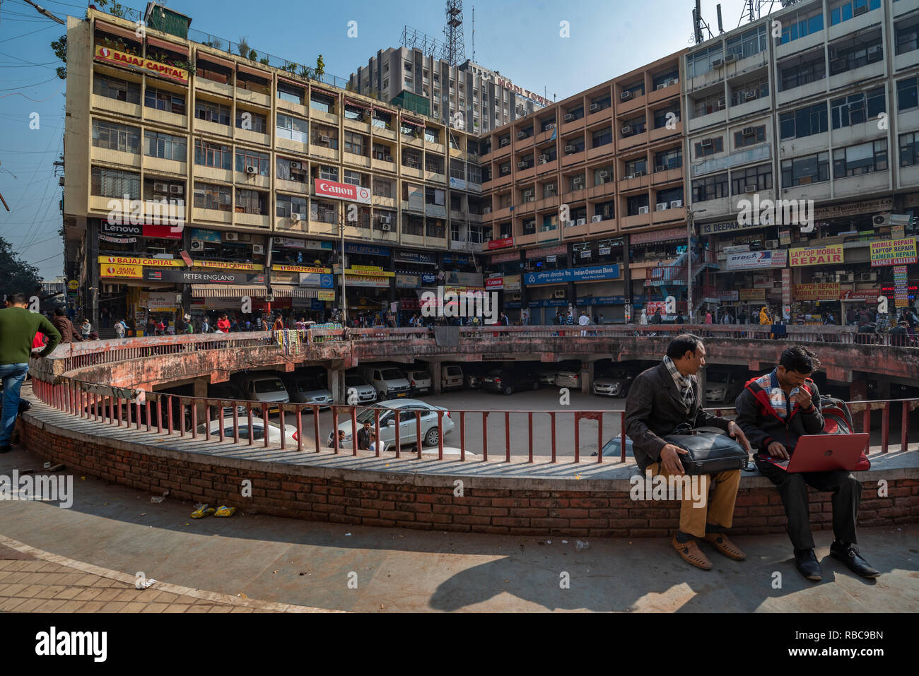 View of a courtyard in Nehru Place, New Delhi, India which is the hub of digital technology: scene shows two people in foreground sitting in the sun. Stock Photo
