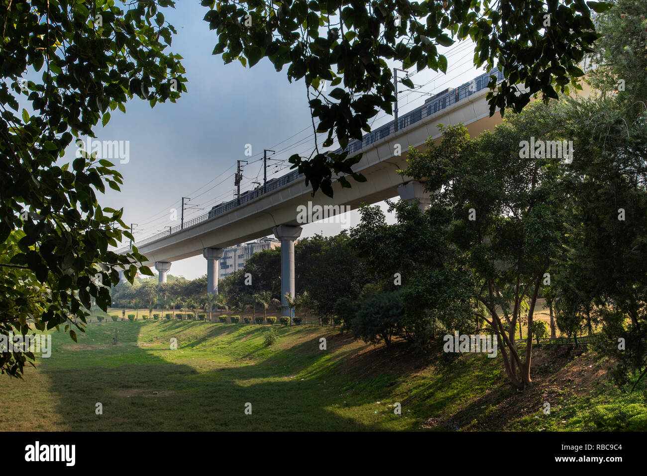View of elevated metro structure from Astha Kunj Park near Nehru Place framed by trees with Metro train going towards Badarpur, New Delhi, India Stock Photo