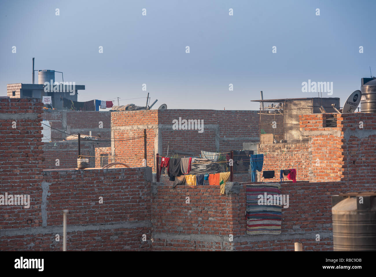 A sunny rooftop scene in JJ Colony Madanpur Khadar, New Delhi making a landscape of satellites dishes and water tanks with clothes drying. Stock Photo