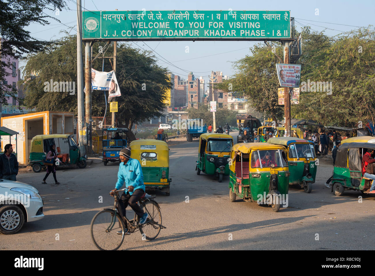 Welcome sign to JJ Colony Madanpur Khadar forms a gateway to the colony framing the entrance road busy with auto-rickshaws and other traffic. New Delhi. Stock Photo