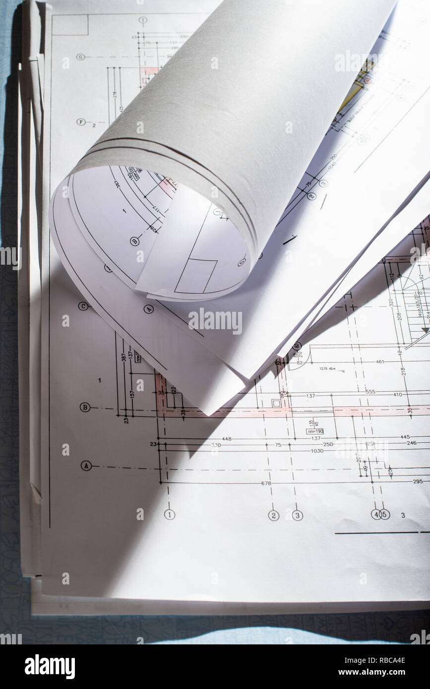 Blueprints on architect desk. Stacked and rolled up architectural projects on natural window light. Construction and building concept. Stock Photo