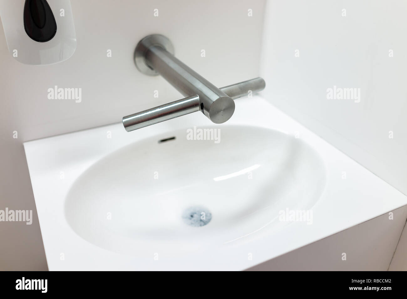 Modern sink in public toilet with soap dispenser, clean white minimalist background interior with metal faucet closeup Stock Photo