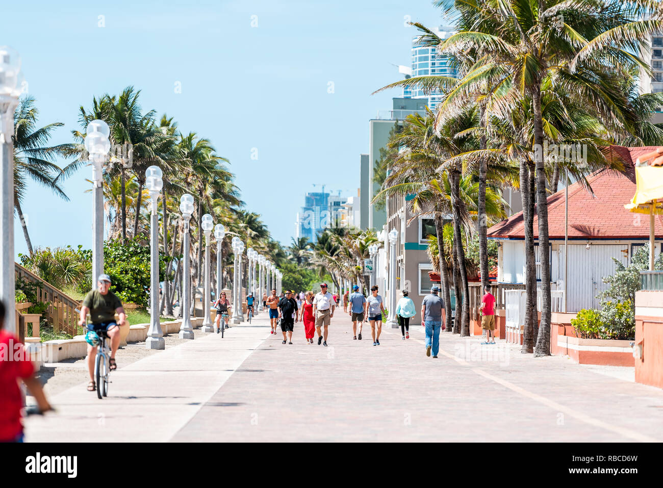 Hollywood, USA - May 6, 2018: Beach boardwalk in Florida Miami cityscape with sunny day and people walking on promenade coast by riding bikes exercisi Stock Photo