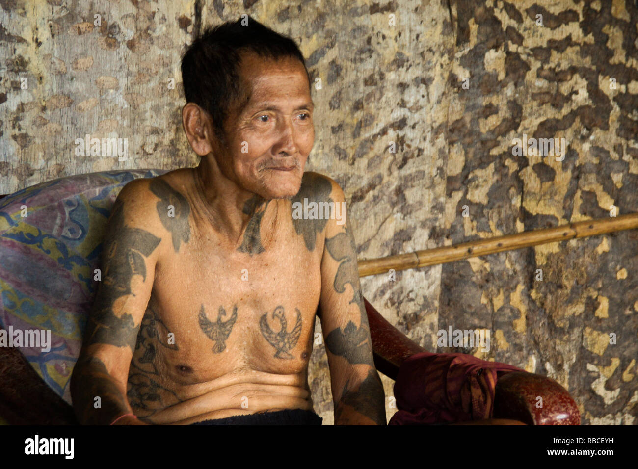 Elderly Iban man with tribal tattoos sitting in chair in communal area of Mengkak Longhouse, Batang Ai, Sarawak (Borneo), Malaysia Stock Photo
