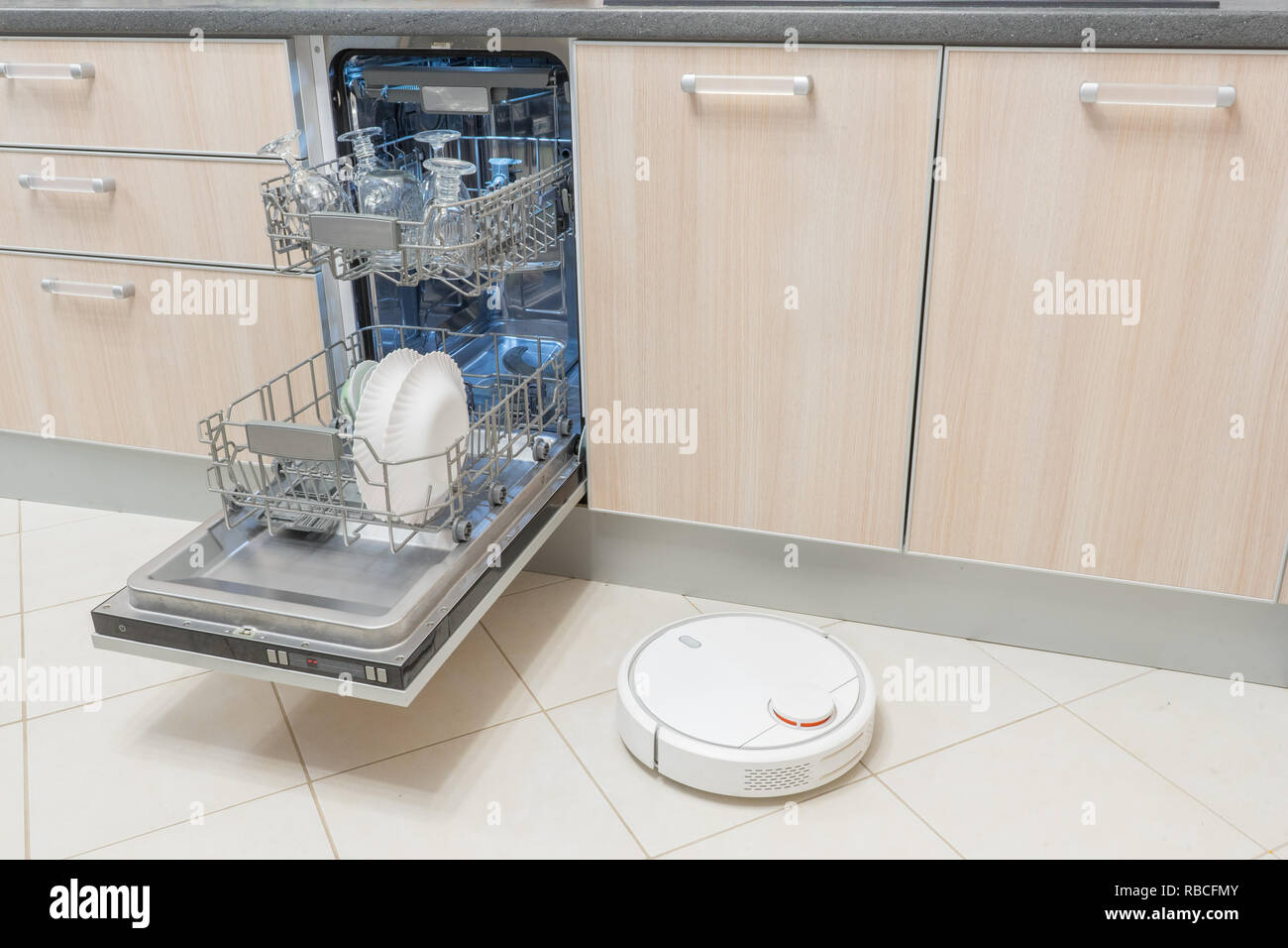 Open dishwasher and Robot vacuum cleaner in kitchen. Modern smart