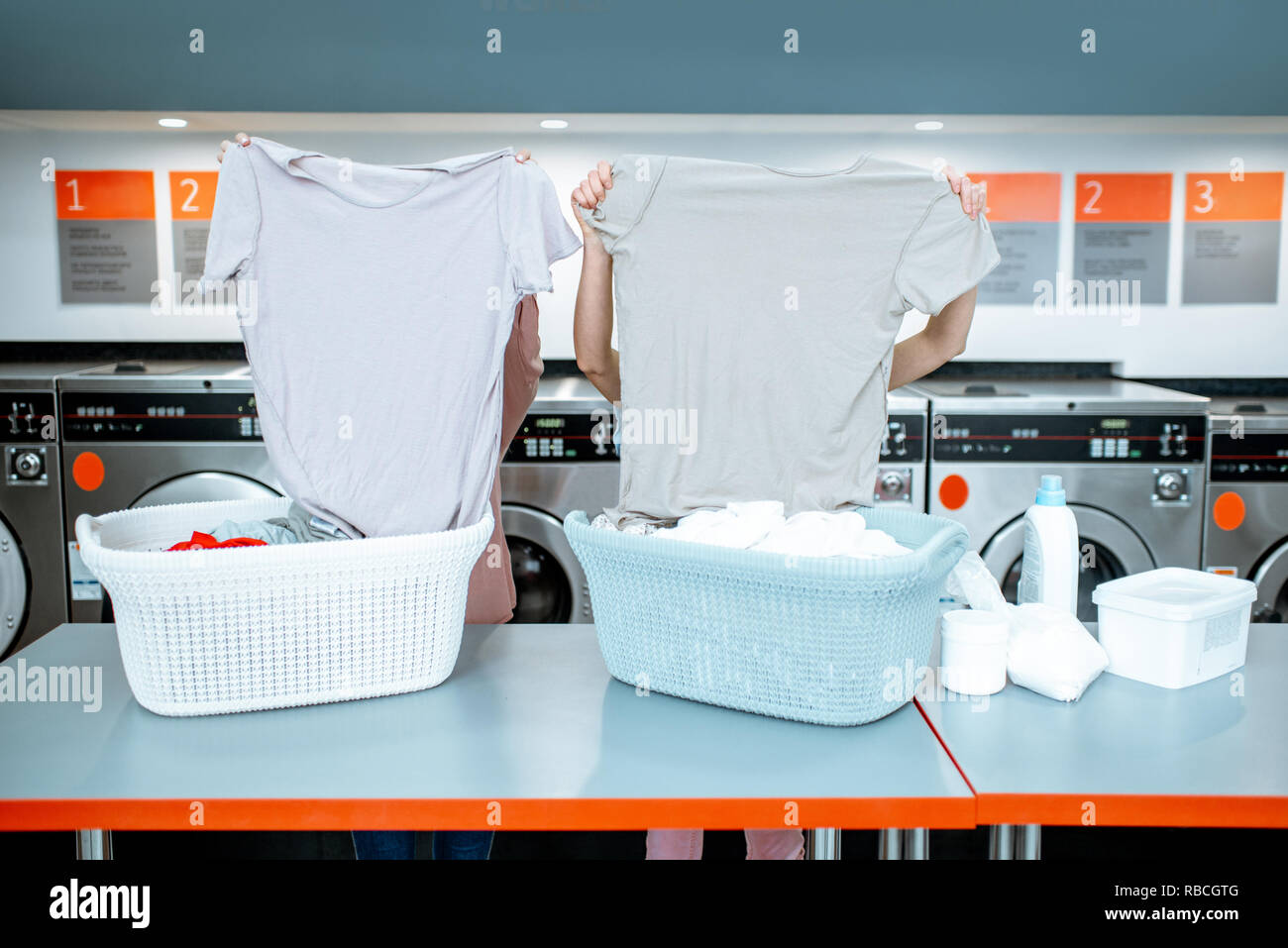 Women sorting clothes near the table with baskets in the self service laundry, closing face with t-shirts Stock Photo